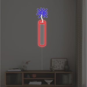 Può includere: Una luce al neon rossa a forma di dinamite con una stella blu in cima. L'insegna al neon è montata su una parete grigia sopra un mobile in legno con decorazioni.