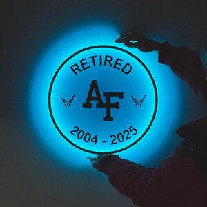May include: A blue glowing circle with the text "RETIRED AF 2004 - 2025" and two wing symbols on either side of the "AF".