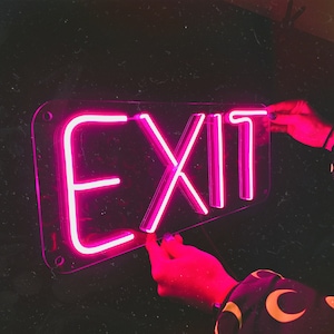 May include: A pink neon sign with the word "EXIT" in a clear acrylic frame.