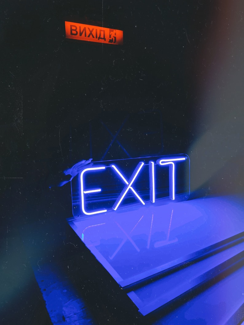 May include: A blue neon sign with the word "EXIT" in white letters. The sign is mounted on a black surface and is reflected in a glass surface.