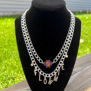 May include: A silver chain necklace with a star charm and the word "FLOWMI" spelled out in gold letters.