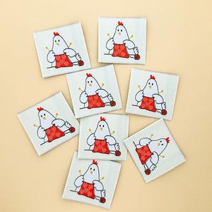 May include: A collection of square white fabric labels featuring a cartoon chicken knitting. The chicken is white with a red comb and is wearing a red sweater. The labels are arranged on a light tan background.