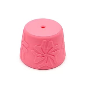 May include: A bright pink, truncated cone-shaped object featuring a raised, embossed floral pattern on its exterior surface. The top of the object is flat and circular, containing a single, small, centered hole that extends through the structure.