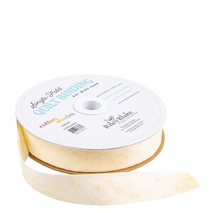 May include: A spool of cream-colored single-fold quilt binding tape. The label reads "Single-Fold Quilt Binding" and "Cotton Shades Cream". The tape is 2.25 inches wide and made of 100% cotton.