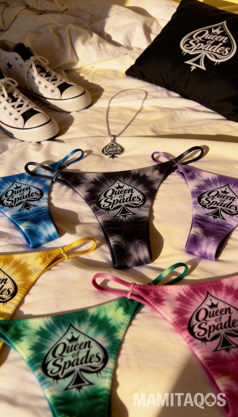 May include: A collection of tie-dye thong underwear in various colors, including blue, black, yellow, green, and pink, each with the "Queen of Spades" logo. A matching necklace and a black pillow with the same logo are also visible.