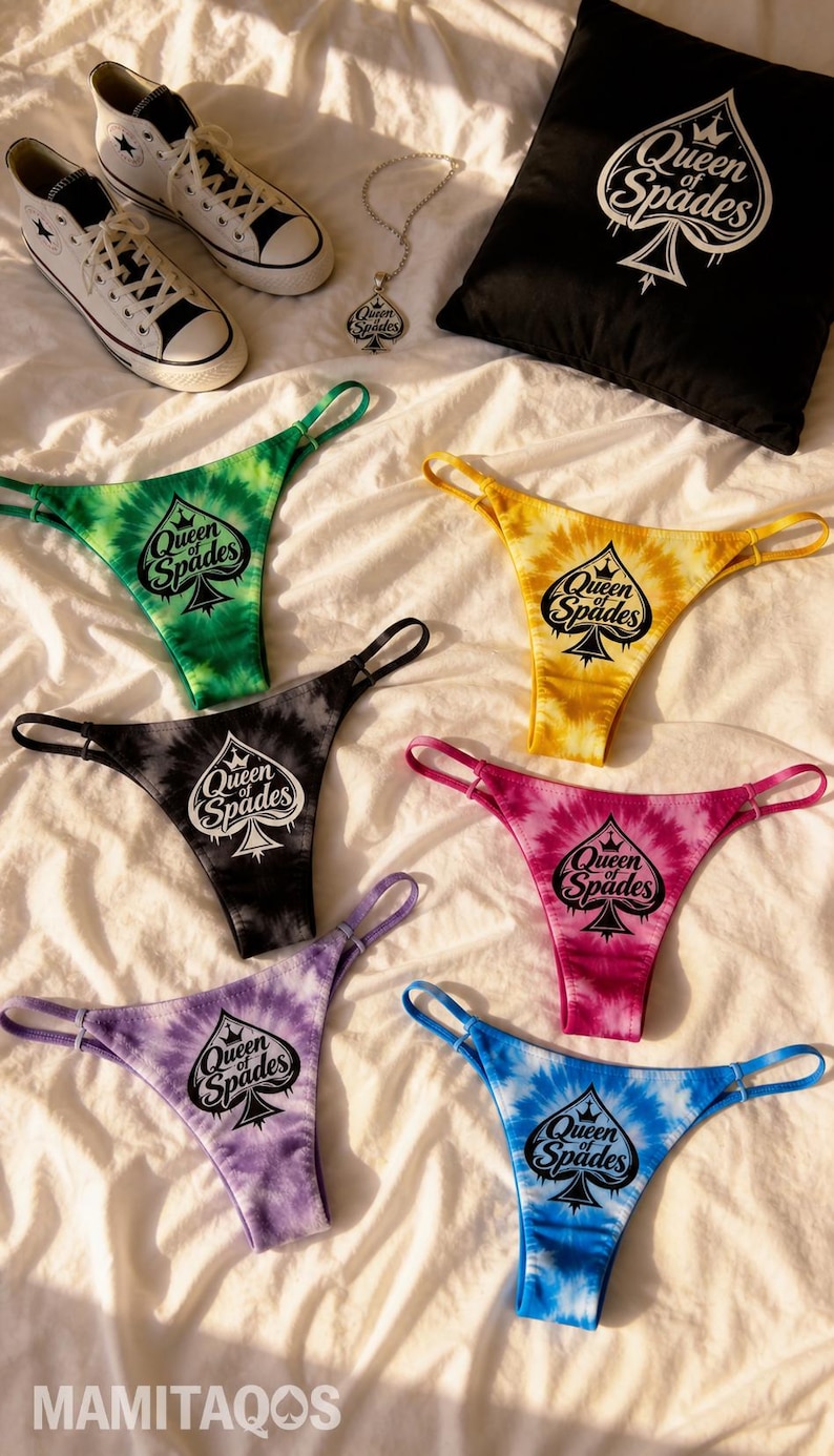 May include: A collection of tie-dye thong underwear in various colors, including green, yellow, black, pink, purple, and blue, each with a spade logo and the text "Queen of Spades". Also, a black pillow, a necklace, and white sneakers.