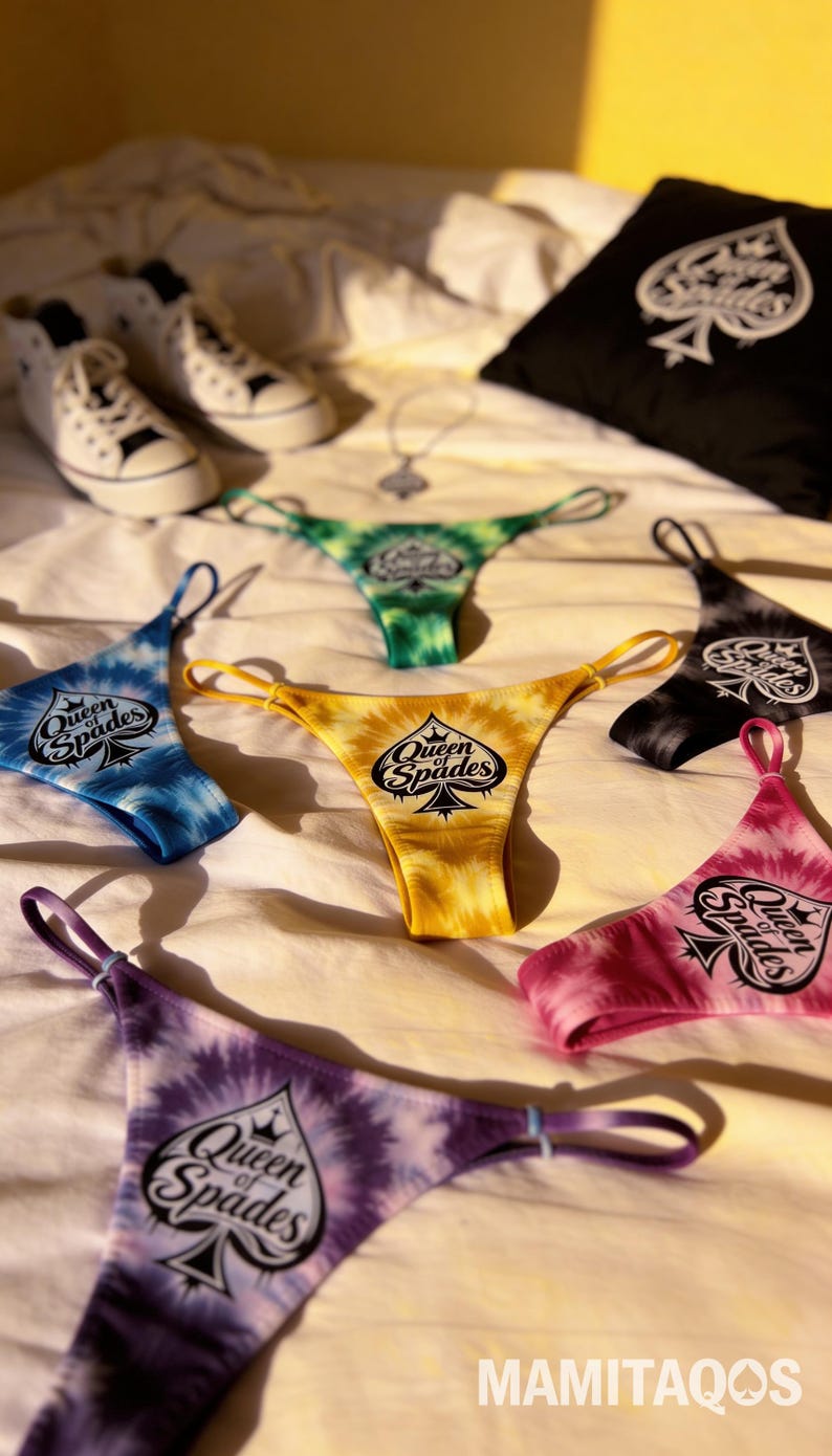 May include: A collection of tie-dye thong underwear in various colors, including blue, yellow, green, black, pink, and purple, each with the text "Queen of Spades" and a spade symbol. A black pillow with a spade symbol and white sneakers are also visible.