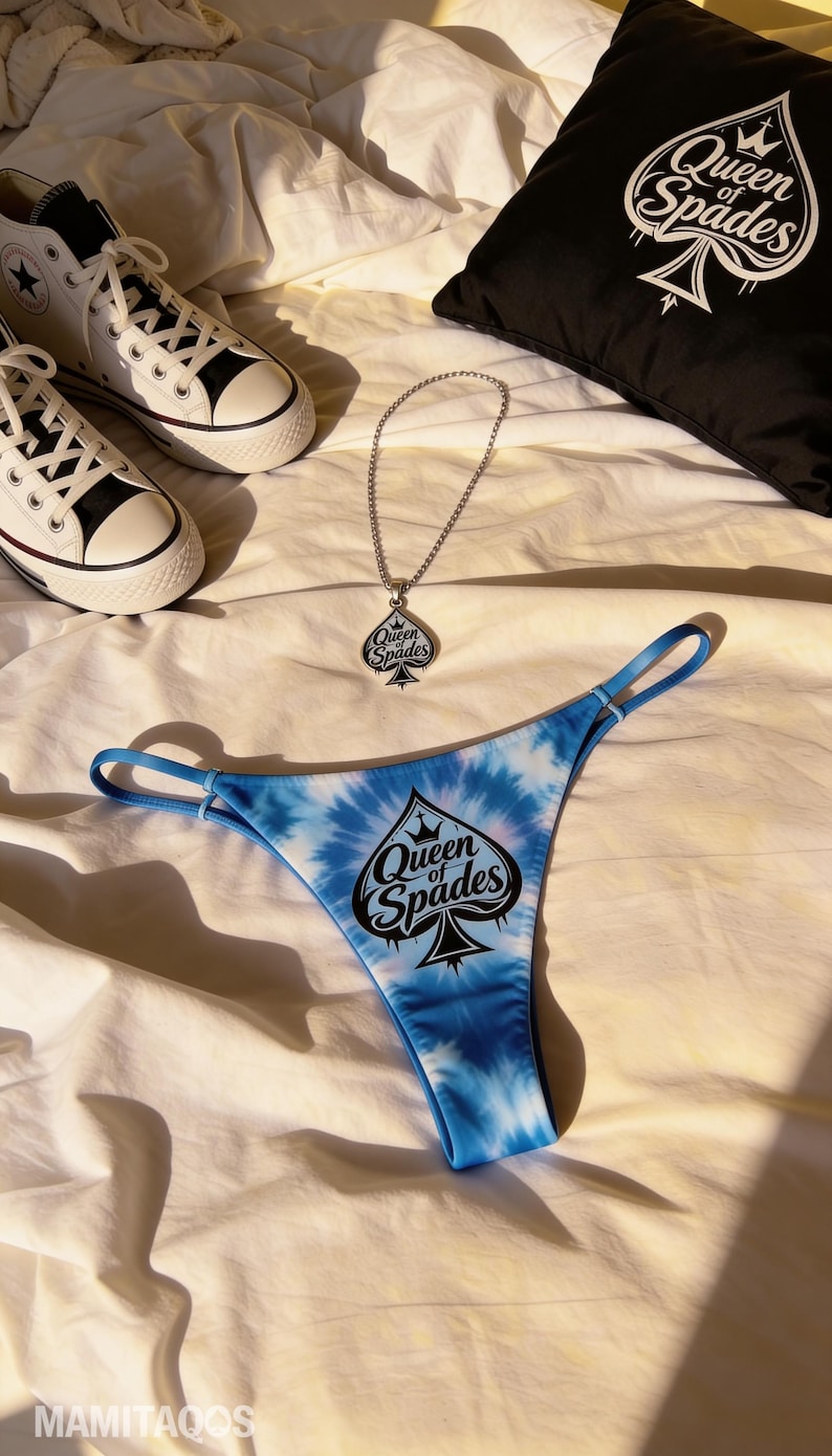 May include: A blue tie-dye thong with the text "Queen of Spades" and a spade graphic, a silver necklace with a matching pendant, a black pillow with the same design, and white high-top sneakers.