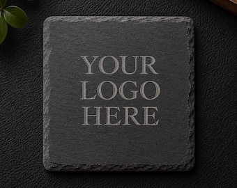May include: A square black slate coaster with rough, natural edges. The center of the coaster features the engraved text "YOUR LOGO HERE" in a serif font. The surface of the stone has a textured, matte finish, providing a dark, neutral base.
