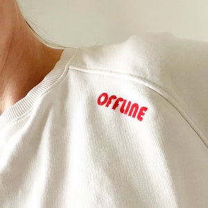 Könnte beinhalten: Weißer Pullover mit dem Wort "OFFLINE" in Rot auf der Schulter gestickt.