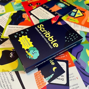 May include: A navy blue box set of "Scribble" cards with the text "where art and mind meet." The box features a cartoon character and the text "36 activities to draw, journal, and reflect." Colorful cards are scattered around the box.