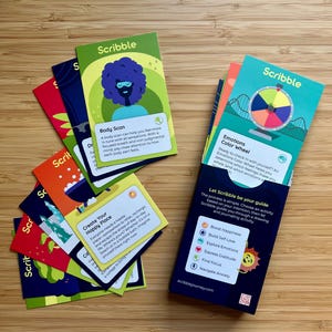 May include: A collection of colorful Scribble cards with illustrations and text, including "Body Scan" and "Emotions Color Wheel." The cards are designed for drawing and journaling activities, with a focus on boosting happiness and exploring emotions.
