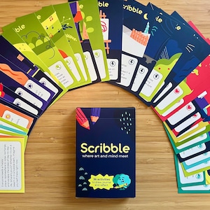 May include: A deck of "Scribble" cards with a navy blue box, featuring the text "Scribble where art and mind meet". The box also states "36 activities to draw, journal and reflect". The cards are arranged in an arc, with colorful illustrations.