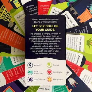 Illustrated card deck displaying drawing and journaling activities for mental health. Card in center shows the emotions targeted: anxiety, focus, gratitude, happiness, and confidence