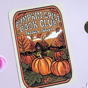 May include: A rectangular sticker with the text "PUMPKIN SPICE BOOK CLUB Readers Retreat." The sticker features an illustration of pumpkins, trees, and a cabin. The color palette includes orange, brown, and green.
