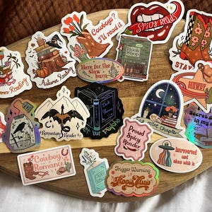 K&ouml;nnte beinhalten: Eine Sammlung bunter Aufkleber mit verschiedenen Designs zum Thema B&uuml;cher. Die Aufkleber enthalten S&auml;tze wie "Spicy Reads", "Cowboy Romance", "Secret Gardens in My Mind" und "Here for the Slow Burn".
