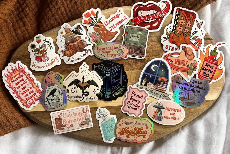 K&ouml;nnte beinhalten: Eine Sammlung bunter Aufkleber mit verschiedenen Designs zum Thema B&uuml;cher. Die Aufkleber enthalten S&auml;tze wie "Spicy Reads", "Cowboy Romance", "Secret Gardens in My Mind" und "Here for the Slow Burn".