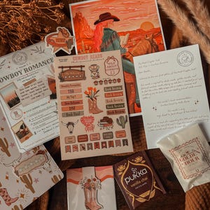 Puede incluir: Una colección de artículos de papelería y accesorios con temática de vaqueros, que incluye pegatinas, una impresión de una persona a caballo y una bolsita de té. Los artículos presentan ilustraciones de botas, cactus y el texto "COWBOY ROMANCE" y "COWBOY READS".