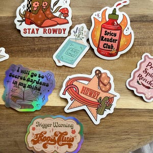 K&ouml;nnte beinhalten: Eine Sammlung bunter Sticker mit verschiedenen buchbezogenen Themen. Die Sticker zeigen S&auml;tze wie "Stay Rowdy", "Spicy Reader Club", "I will go to Secret Gardens in my mind", "Howdy", "Proud Spicy Reader" und "Trigger Warning Book Time".
