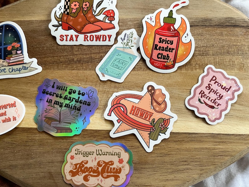 K&ouml;nnte beinhalten: Eine Sammlung bunter Sticker mit verschiedenen buchbezogenen Themen. Die Sticker zeigen S&auml;tze wie "Stay Rowdy", "Spicy Reader Club", "I will go to Secret Gardens in my mind", "Howdy", "Proud Spicy Reader" und "Trigger Warning Book Time".