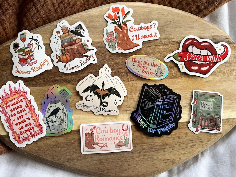 K&ouml;nnte beinhalten: Eine Sammlung bunter Aufkleber mit verschiedenen Buchmotiven. Die Aufkleber zeigen Illustrationen von B&uuml;chern, Cowboys, einem Drachen, einem Buchladen, einer Chilischote und einer Teetasse. Der Text auf den Aufklebern lautet "Summer Reading", "Autumn Reading", "Romantasy Reader", "Sweet but Psycho", "Spicy Reads", "Here for the Slow Burn", "Proudly Going So Hell For What's On My Kindle", "Cowboys? I'll Read It", und "Cowboy Romance".