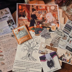 May include: A collection of stationery items including a Witching Hour themed print, a tea bag of Ahmad Tea Camomile Honey & Vanilla, a tree illustration, a magnetic bookmark with a cauldron, and various stickers featuring a raven and text.