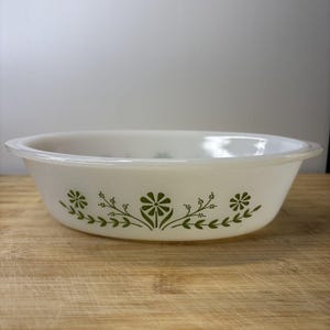 May include: White oval serving dish with a green floral design. The dish has a simple, elegant shape with a slightly raised rim. The floral pattern consists of stylized flowers and leaves, adding a touch of nature to the design.