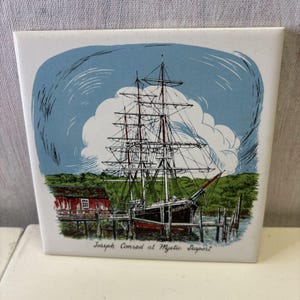 Puede incluir: Azulejo de cerámica cuadrado con una ilustración náutica de un velero atracado en un muelle. La imagen incluye un edificio rojo, follaje verde y un cielo azul con nubes. El texto en la parte inferior dice "Joseph Conrad at Mystic Seaport."