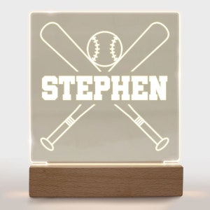 May include: A white personalized night light with a baseball and crossed bats design. The name "STEPHEN" is written in white letters on the light.