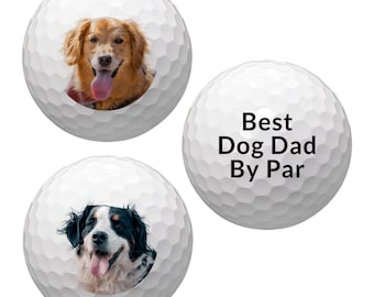 May include: Three white golf balls with images printed on them. One ball has a golden retriever dog with its tongue sticking out. Another ball has a Bernese Mountain Dog with its tongue sticking out. The third ball has the text "Best Dog Dad By Par" printed on it.