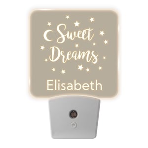 May include: A beige night light with a white inscription that reads "Sweet Dreams" and the name "Elisabeth" surrounded by white stars. The night light has a white plastic base with an on/off switch.