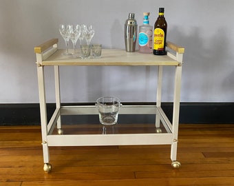 Vintage hand painted bar cart on wheels. Solid wood with a new 2” glass shelf. Beige with gold accents.