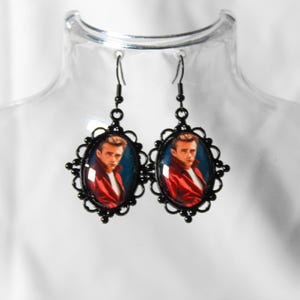 Op de afbeelding: Een paar zwarte oorhangers met ovale portretten van een man in een rode jas tegen een blauwe achtergrond. De portretten zijn omlijst door sierlijke zwarte filigraan. De oorbellen hangen aan zwarte oorhaken.