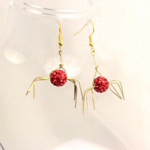 May include: A pair of gold spider earrings with red rhinestone accents.
