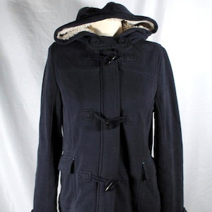 May include: A navy blue hooded duffel coat with a toggle closure. The coat has a hood lined with a cream-colored, fuzzy material. The coat has two front pockets and a button closure at the neck.