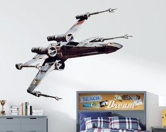 May include: A gray twin-sized bed with a blue and white plaid comforter and a headboard featuring a corkboard with the words "Beach Dream" and photos. A gray dresser with 12 drawers is on the left side of the image. A Star Wars X-Wing fighter decal is on the wall above the bed.