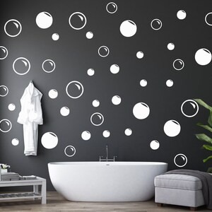 May include: A white bathtub with a white towel hanging on the wall behind it. The wall is dark gray and has white bubble stickers on it. There is a green plant in a pot on the right side of the image.