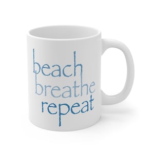 May include: White ceramic mug featuring the words "beach breathe repeat" in blue script. The mug has a curved handle and a simple design. Ideal for tea, coffee, or any preferred drink.