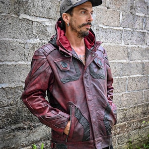 May include: A burgundy leather jacket with black leather accents and a hood. The jacket has a zipper closure and multiple pockets. The jacket is worn by a person with a black and grey patterned cap.