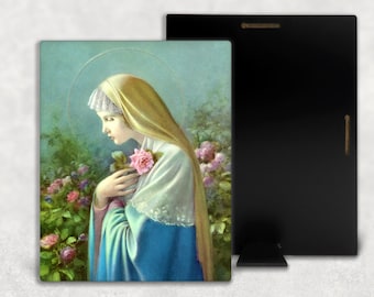 May include: A painting of the Virgin Mary in a blue robe and white veil, holding a pink rose in her hand. She is standing in a garden with green foliage and pink roses.