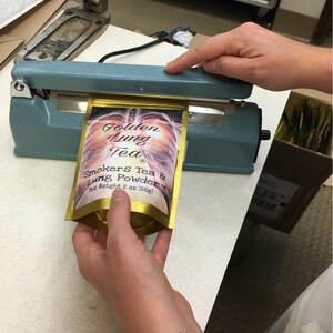 Pu&ograve; includere: Una bustina dorata con un'immagine di un paio di polmoni e il testo "Golden Lung Tea" e "Smokers Tea & Lung Powder" con un peso netto di 2 oz (56g).