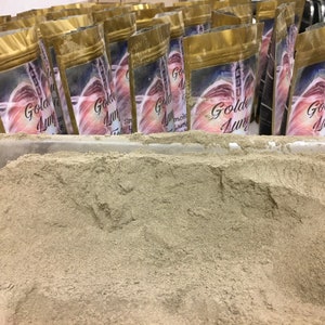 Pu&ograve; includere: Un mucchio di polvere marrone chiaro in un contenitore bianco. La polvere &egrave; circondata da pi&ugrave; sacchetti di alluminio dorato con la scritta "Golden Lung" stampata su di essi.