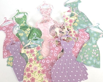 May include: A collection of paper dress cutouts in various pastel colors, including pink, green, and lavender. The dresses feature floral and polka dot patterns, and each has a small hanger at the top. The overall theme is vintage and feminine.