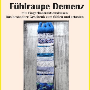 May include: A sensory toy with a blue hand-shaped top and a long, textured body. The body is made of various fabrics, including lace and patterned materials. The text "Fühlraupe Demenz" is at the top.