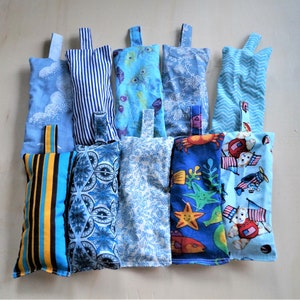 Puede incluir: Una colección de 10 bolsas de tela azul y blanca con varios patrones. Las bolsas están llenas de arroz o frijoles y se utilizan para la relajación y el alivio del estrés.