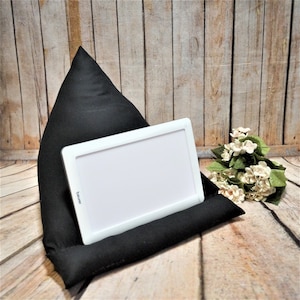 Könnte beinhalten: Schwarzes dreieckiges Kissen mit einem weißen Tablet-Ständer. Der Tablet-Ständer hat den Schriftzug "beamer" aufgedruckt. Das Kissen liegt auf einer Holzoberfläche.