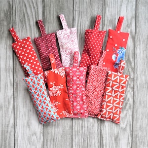 Puede incluir: Una colección de 10 bolsas de tela roja y blanca con diferentes patrones. Las bolsas tienen un lazo en la parte superior para colgar.