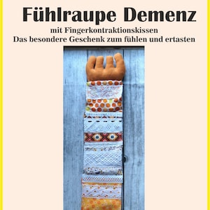 May include: A sensory toy with the text "Fühlraupe Demenz" and additional text. The toy features a brown, hand-shaped top and a long, colorful body made of various patterned fabrics, including lace and polka dots. The background is a light blue wooden surface.