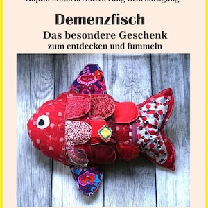 May include: A plush fish toy featuring a red body with various fabric patches in floral, heart, and geometric patterns. The fish has a white eye, multiple layered fabric flaps, and a tail with a red, white, and black polka dot design.