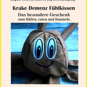 May include: A brown octopus-shaped sensory pillow with embroidered blue eyes and a smiling mouth. The pillow has the text "Krake Demenz Fühlkissen" and other German text. The image is a close-up of the pillow.